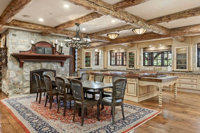 Spacious dining area featuring exposed wood beams, a stone fireplace with a wood mantel, wood-finish flooring, and built-in cabinetry