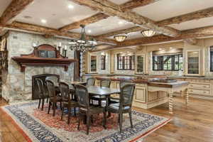 Spacious dining area featuring exposed wood beams, a stone fireplace with a wood mantel, wood-finish flooring, and built-in cabinetry