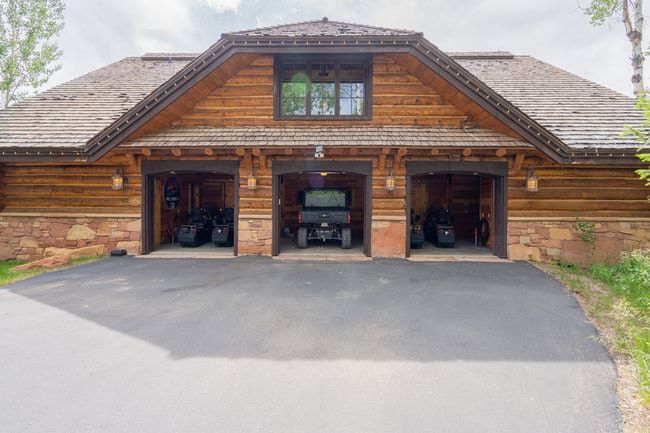 Three-bay garage with wood siding and stone accents, featuring a shingle roof, a second-story window, and exterior wall lanterns