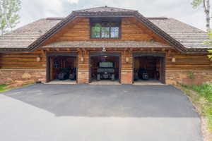 Three-bay garage with wood siding and stone accents, featuring a shingle roof, a second-story window, and exterior wall lanterns