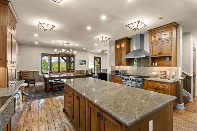Kitchen featuring a large island with stone countertop, stainless steel range with hood, wood-finish cabinetry, and wood-finish flooring