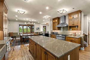 Kitchen featuring a large island with stone countertop, stainless steel range with hood, wood-finish cabinetry, and wood-finish flooring