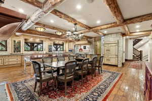 Spacious kitchen and dining area with exposed wood ceiling beams, wood-finish flooring, custom cabinetry, stone accent walls, and an integrated paneled refrigerator