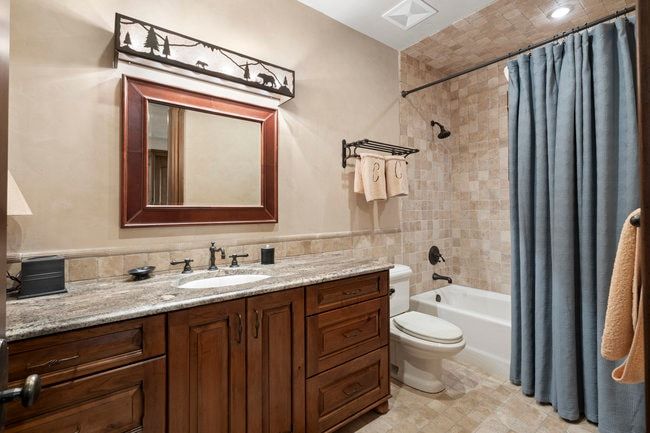 Vanity with granite countertop and integrated sink, framed mirror, dark wood cabinetry, and a full-size bathtub with tiled surround