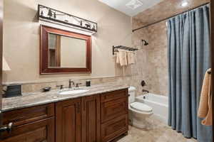Vanity with granite countertop and integrated sink, framed mirror, dark wood cabinetry, and a full-size bathtub with tiled surround