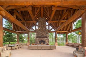 Expansive covered patio featuring a stone fireplace, exposed timber beam ceiling, integrated stone benches, and concrete flooring