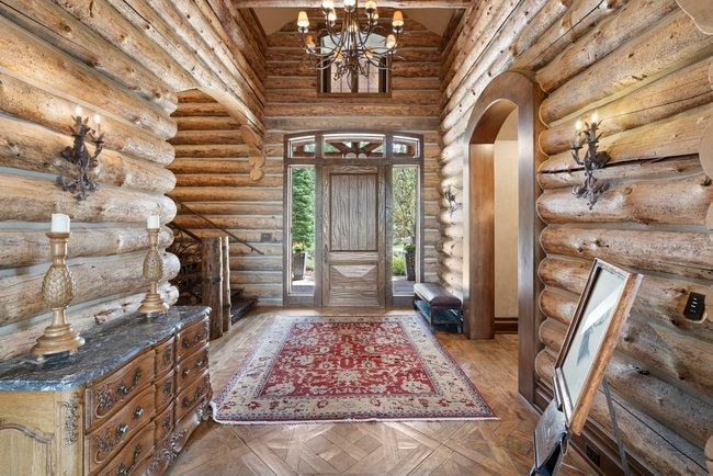 Grand entry hall featuring log construction, a substantial wood front door with sidelight windows, and a coffered ceiling with a central chandelier