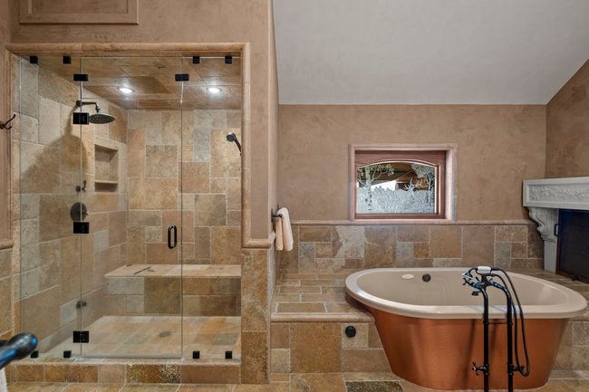 Stone tile bathroom featuring a walk-in shower with a built-in bench, a rain showerhead, a hand-held shower, and a copper-clad soaking tub with an antique-style faucet