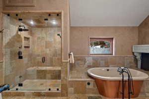 Stone tile bathroom featuring a walk-in shower with a built-in bench, a rain showerhead, a hand-held shower, and a copper-clad soaking tub with an antique-style faucet