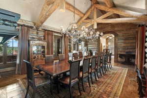 Spacious dining area featuring exposed wood beams, a log wall finish, wood-finish flooring, and multiple windows
