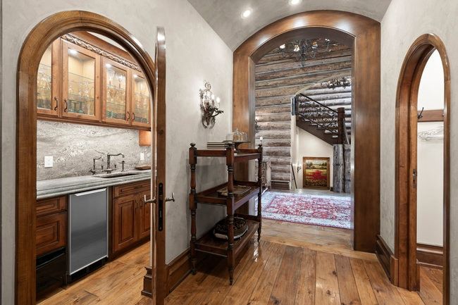 Archways frame a wet bar with wood cabinetry, glass-front upper cabinets, a stone countertop, and a stainless steel undercounter refrigerator