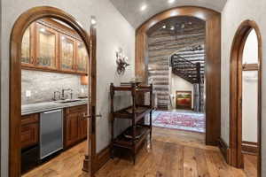 Archways frame a wet bar with wood cabinetry, glass-front upper cabinets, a stone countertop, and a stainless steel undercounter refrigerator