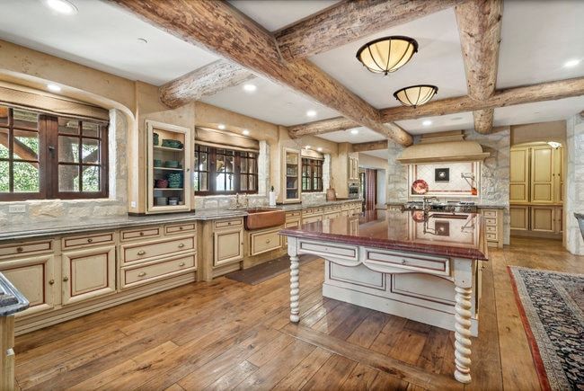Rustic kitchen featuring exposed wood beams, light-toned custom cabinetry, wood-finish flooring, a central island with a polished countertop, and a built-in copper farmhouse sink
