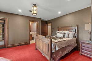 Recessed lighting and a central pendant fixture illuminate a room featuring patterned wallpaper, red textured carpeting, and detailed wood trim