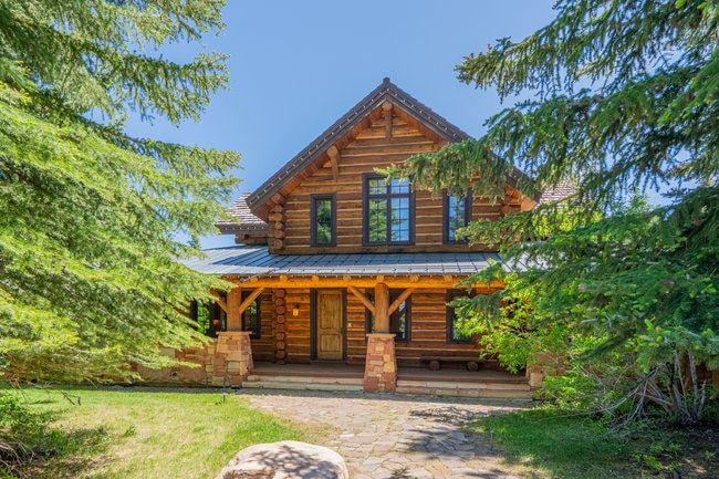 Rustic log cabin exterior featuring a multi-gabled roofline and a stone-clad porch