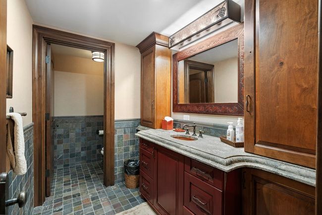 Bathroom featuring a rich wood-tone vanity, stone countertop, and an ornate framed mirror