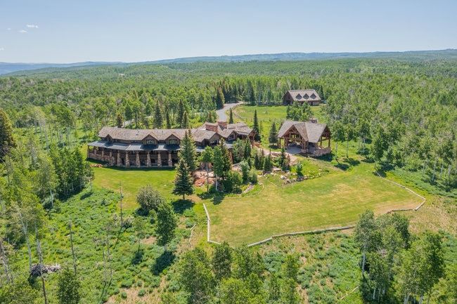 Expansive property featuring multiple structures, including a primary residence with stone and log detailing, a detached outbuilding, and a separate covered pavilion