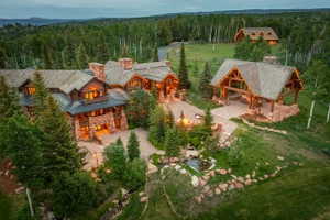 Expansive stone and log construction residence featuring multiple gabled roofs, an outdoor covered pavilion with exposed timber framing, a stone fire pit, and a naturalistic water feature