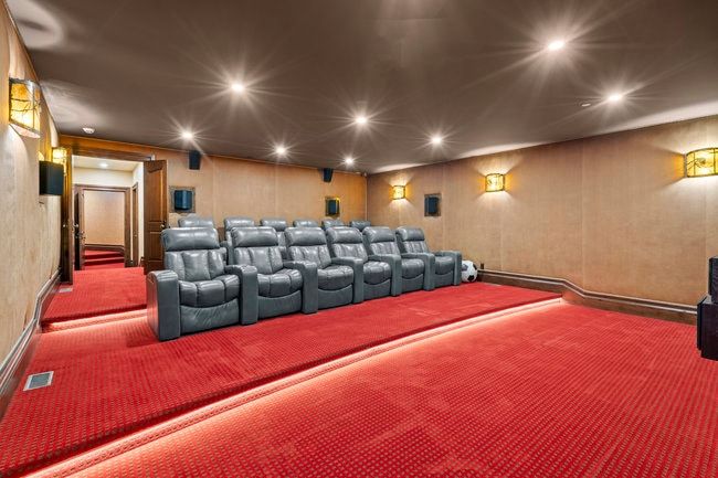 Dedicated home theater featuring tiered seating, red carpet flooring with illuminated risers, recessed ceiling lighting, and wall-mounted sconces