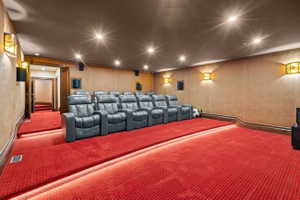 Dedicated home theater featuring tiered seating, red carpet flooring with illuminated risers, recessed ceiling lighting, and wall-mounted sconces