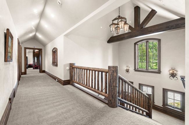 Vaulted ceiling hallway with warm wood trim and light-colored carpet