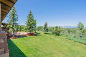 Expansive green lawn framed by mature trees, featuring a stone patio and natural wood deck