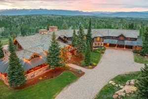 Expansive log and stone estate featuring multiple gabled rooflines, a paver driveway, and mature evergreen trees