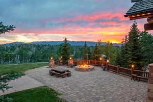 Expansive paver patio featuring a built-in stone fire pit, wood railing, and stone pillars