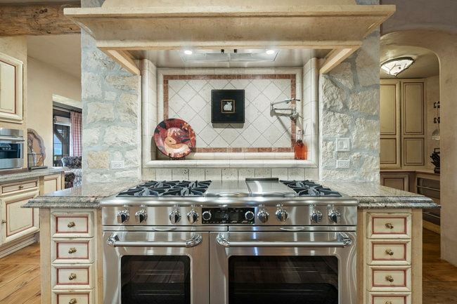 Stainless steel range with double ovens set into a stone and wood-finish range hood