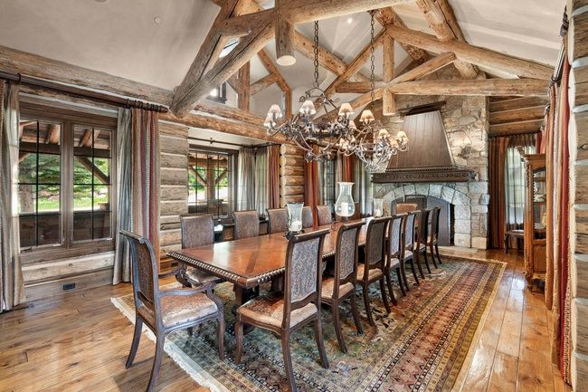 Spacious dining area featuring exposed timber trusses, a stone fireplace, wood-finish flooring, and multiple windows