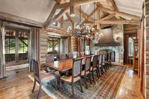 Spacious dining area featuring exposed timber trusses, a stone fireplace, wood-finish flooring, and multiple windows