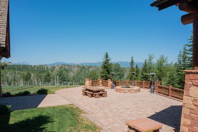 Expansive paver patio featuring a stone fire pit, wood railing, and stone pillars