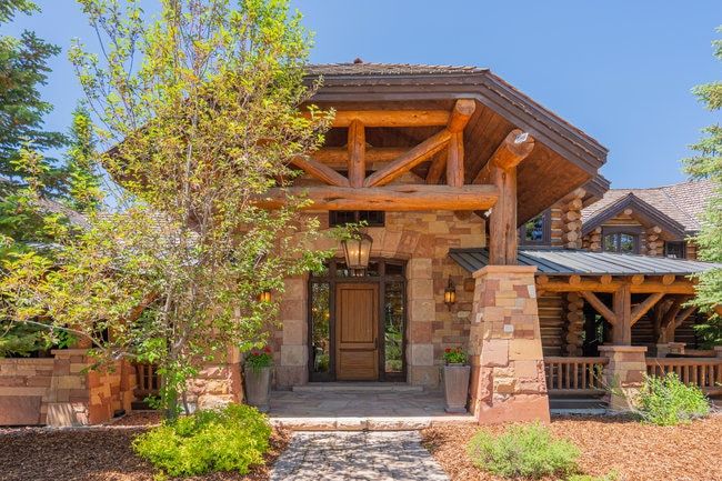 Stone and timber frame entry featuring a natural wood door with sidelights, decorative outdoor lighting, and a paved walkway