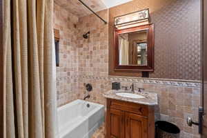 Bathroom with tile surround tub/shower combination, decorative tile wainscoting, a vanity with stone countertop, and a framed mirror with an overhead light fixture