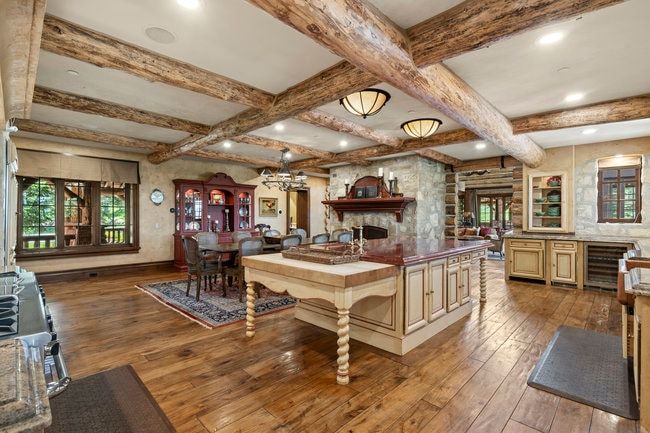 Open concept living space featuring exposed wood beams, wood-finish flooring, a stone accent wall with built-in oven, and a kitchen island with a stone countertop