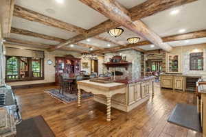 Open concept living space featuring exposed wood beams, wood-finish flooring, a stone accent wall with built-in oven, and a kitchen island with a stone countertop