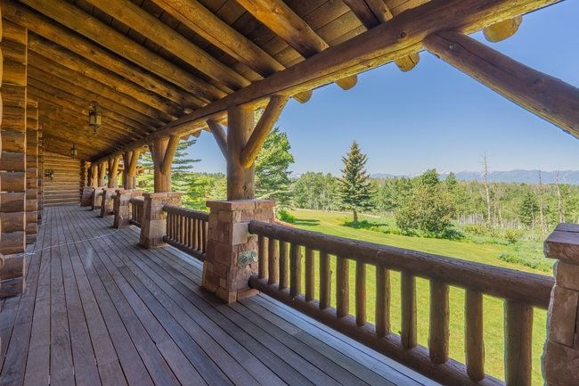 Expansive covered porch featuring wood-finish flooring, log beam ceiling, log railings, and stone pillar accents
