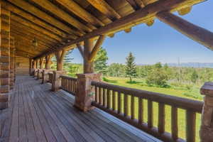Expansive covered porch featuring wood-finish flooring, log beam ceiling, log railings, and stone pillar accents