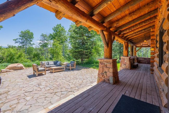 Expansive outdoor living area featuring a stone patio and a covered porch with log beams and stone column bases