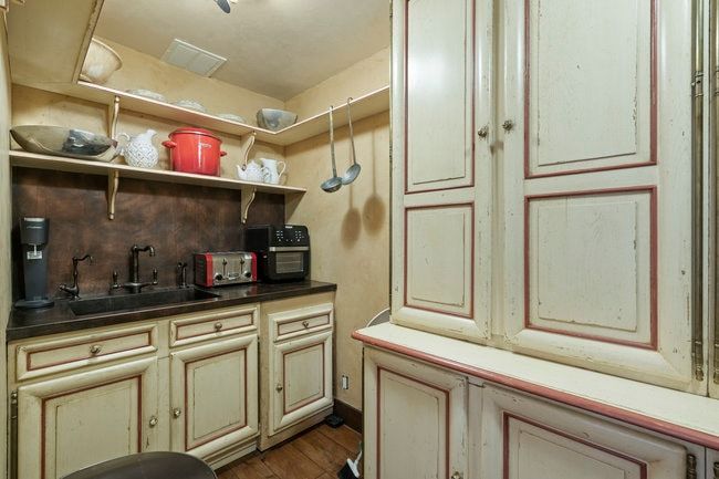 Compact kitchen area featuring a dark countertop, undermount sink with a dark faucet, and light-toned cabinetry with framed paneling
