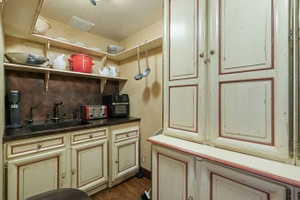 Compact kitchen area featuring a dark countertop, undermount sink with a dark faucet, and light-toned cabinetry with framed paneling