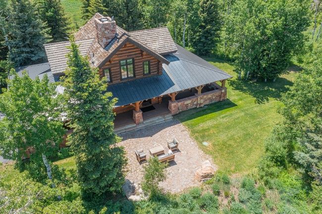 Log cabin-style residence featuring a prominent stone chimney, wood-shake roof, and a covered front porch with stone pillars