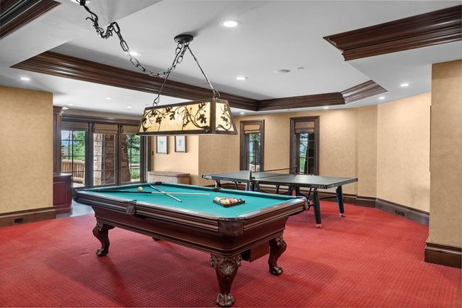 Recreation room featuring red textured carpeting, a tray ceiling with dark wood trim, recessed lighting, and a decorative stained glass chandelier