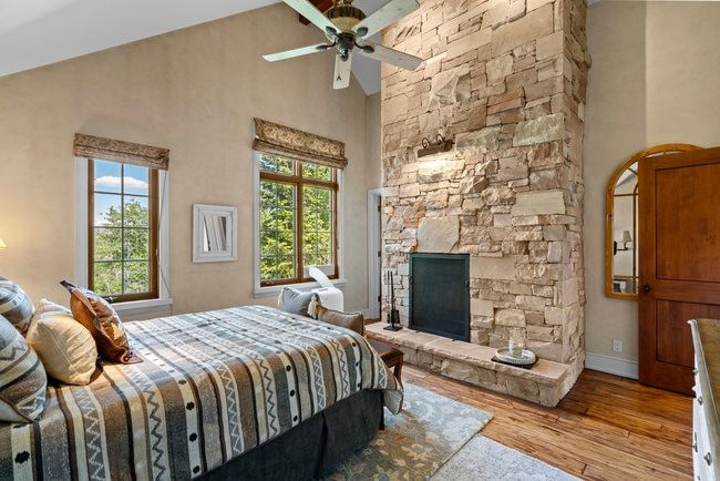 Stone-clad fireplace with hearth, vaulted ceiling, wood-finish flooring, and two double-hung windows