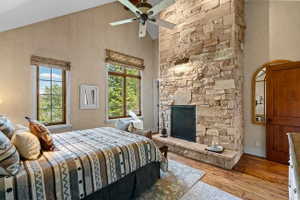 Stone-clad fireplace with hearth, vaulted ceiling, wood-finish flooring, and two double-hung windows