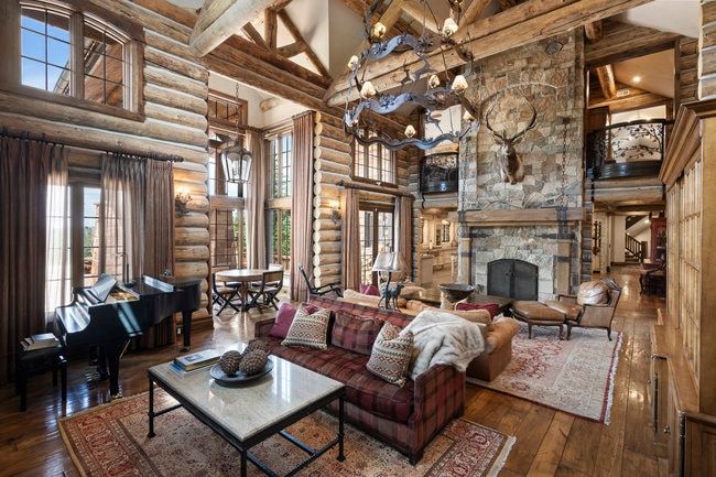 Spacious living area featuring exposed log walls, a stone fireplace, wood-finish flooring, and a grand chandelier