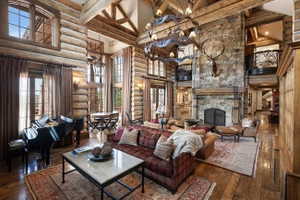 Spacious living area featuring exposed log walls, a stone fireplace, wood-finish flooring, and a grand chandelier