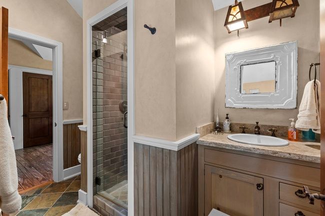 Bathroom featuring a glass-enclosed shower with subway tile, a vanity with an undermount sink, stone-finish countertop, decorative mirror, and an overhead light fixture