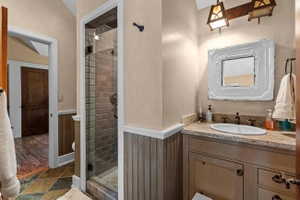 Bathroom featuring a glass-enclosed shower with subway tile, a vanity with an undermount sink, stone-finish countertop, decorative mirror, and an overhead light fixture