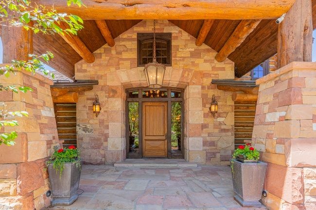 Stone facade entry featuring a solid wood door with sidelights, a flagstone patio, and a covered porch with exposed timber beams